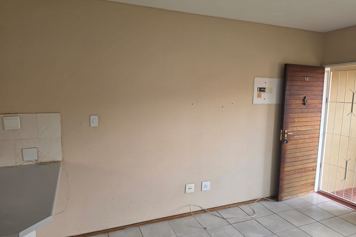 An empty entrance area featuring tiled flooring, a timber front door with security gate, and an exposed electrical distribution board.