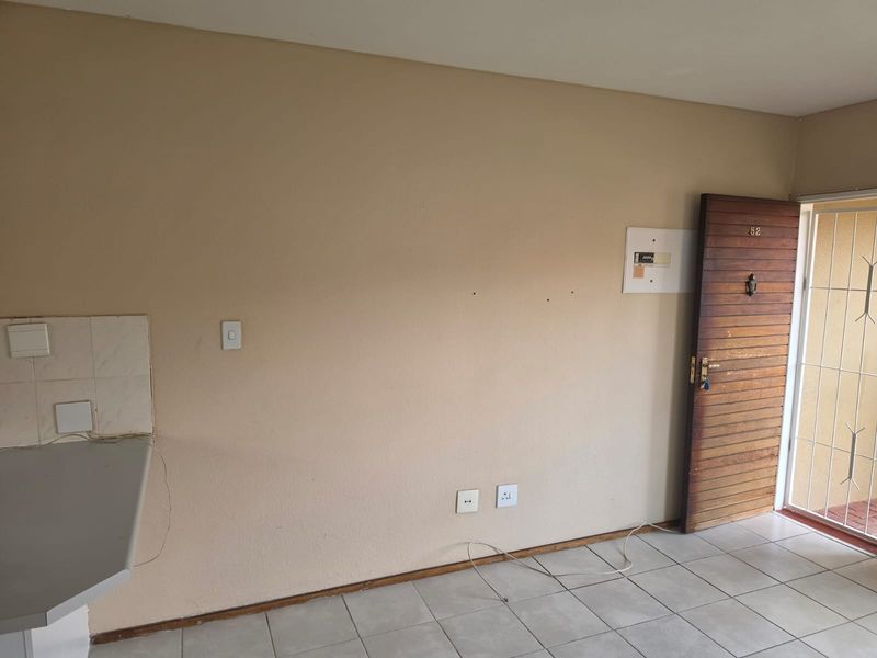 An empty entrance area featuring tiled flooring, a timber front door with security gate, and an exposed electrical distribution board.
