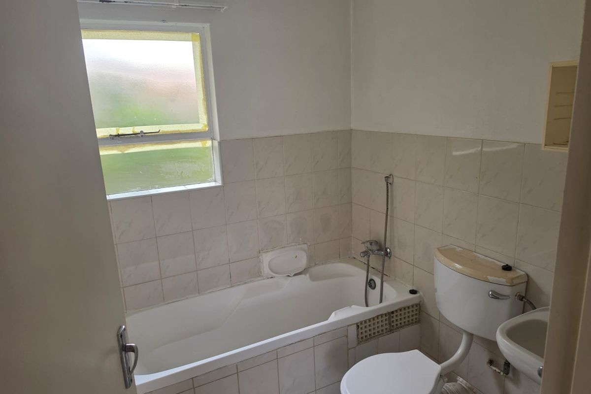 A dated bathroom featuring a standard bathtub, toilet, and washbasin with tiled walls, requiring cosmetic updates and maintenance to improve its overall condition.
