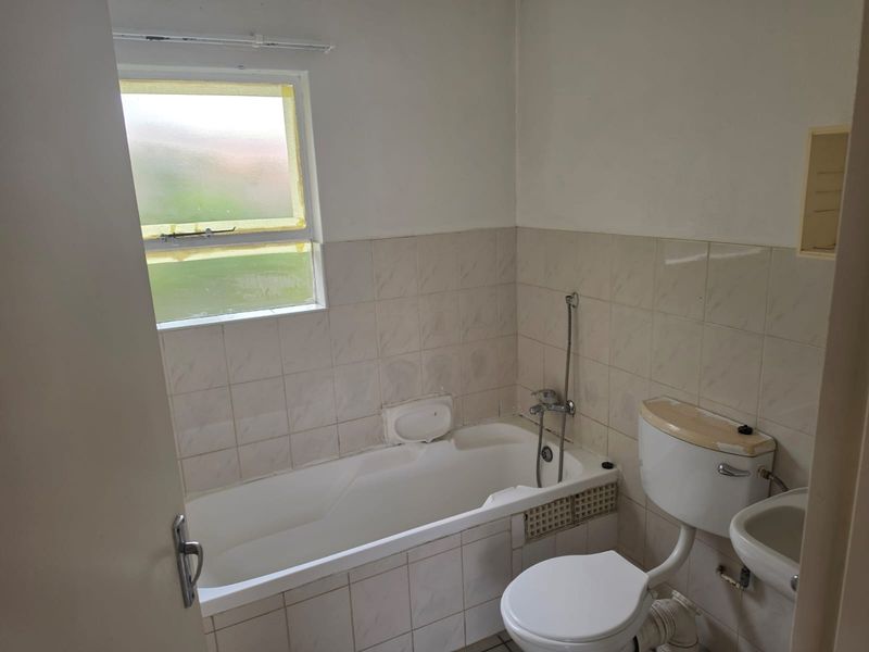 A dated bathroom featuring a standard bathtub, toilet, and washbasin with tiled walls, requiring cosmetic updates and maintenance to improve its overall condition.