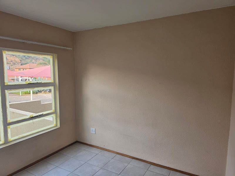 An empty bedroom featuring tiled flooring and a large window with aluminium frames, currently undergoing minor maintenance or painting.