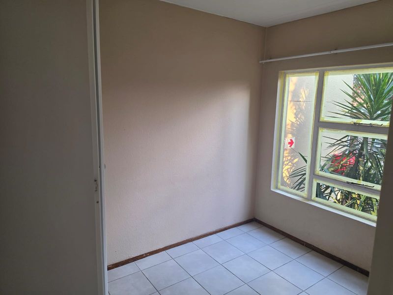 An empty bedroom featuring tiled flooring, a built-in cupboard, and natural light through a large window.