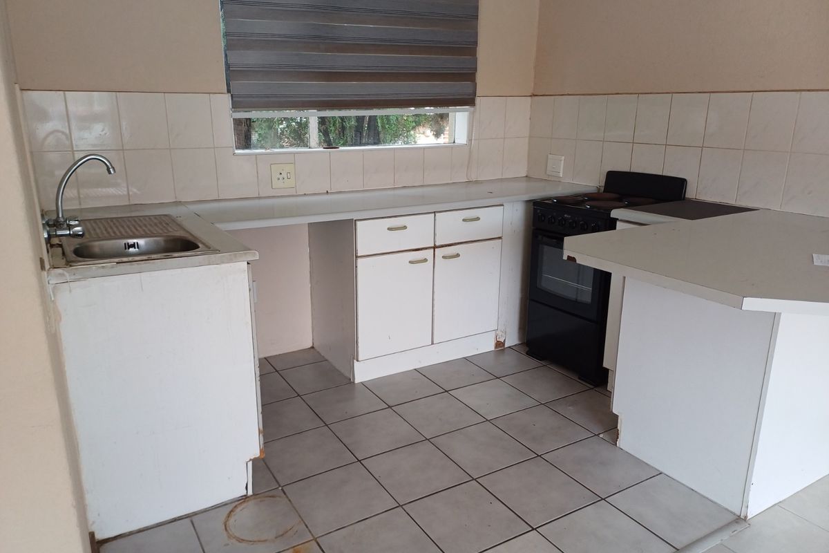 A functional kitchen featuring white cabinetry, tiled flooring, a stainless steel sink, and a freestanding oven, offering a blank canvas for potential renovation.