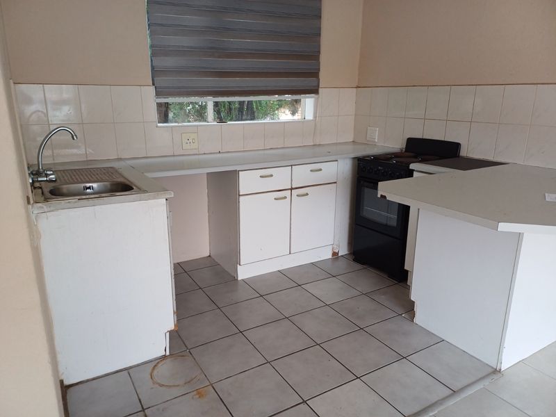 A functional kitchen featuring white cabinetry, tiled flooring, a stainless steel sink, and a freestanding oven, offering a blank canvas for potential renovation.