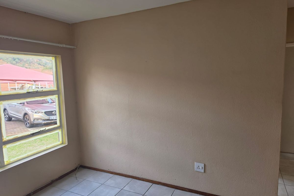 An empty bedroom featuring tiled flooring and a large window with aluminium frames, providing a neutral canvas for potential interior design updates.