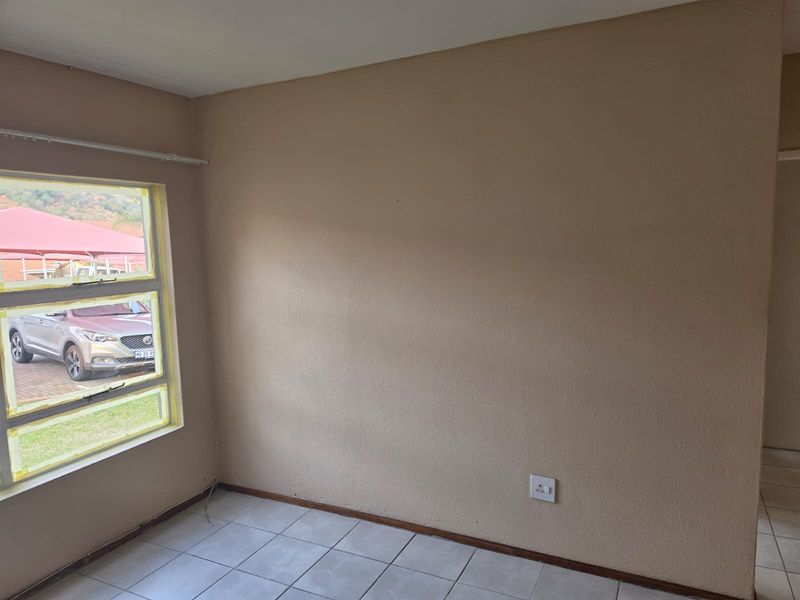 An empty bedroom featuring tiled flooring and a large window with aluminium frames, providing a neutral canvas for potential interior design updates.