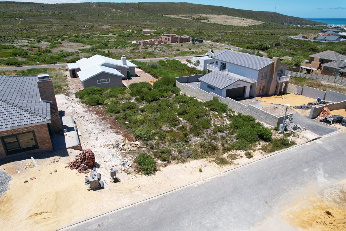 Aerial view of a vacant residential plot situated within a developing coastal neighborhood, featuring surrounding infrastructure and nearby residential properties.
