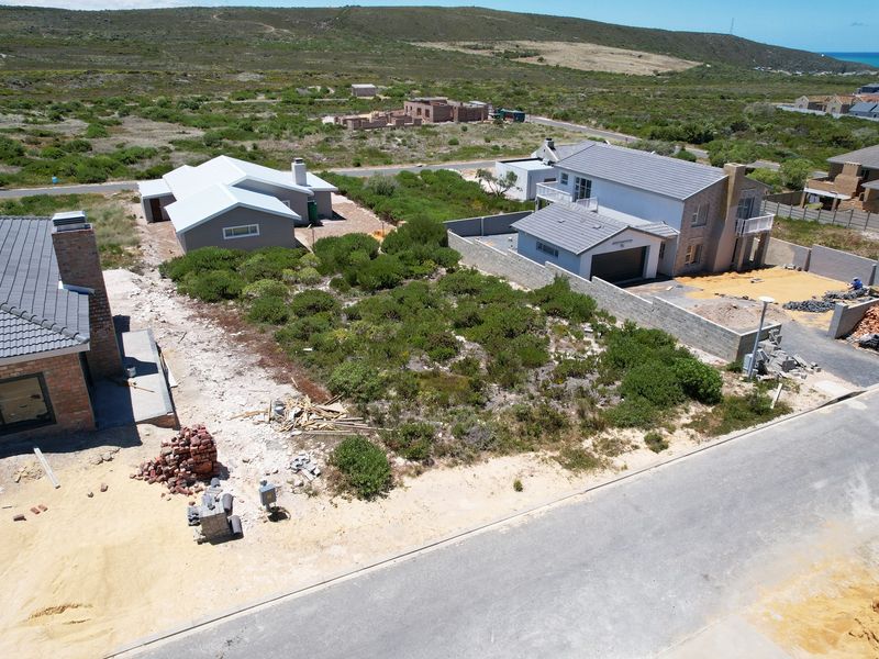 Aerial view of a vacant residential plot situated within a developing coastal neighborhood, featuring surrounding infrastructure and nearby residential properties.