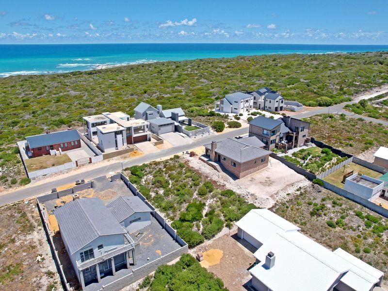 An aerial view of a coastal residential development featuring modern homes, paved streets, and surrounding natural vegetation near the ocean.