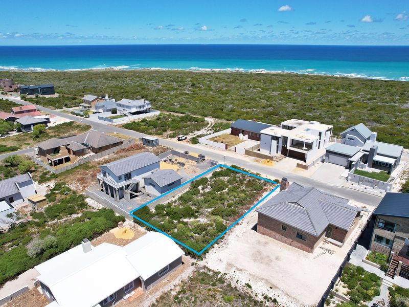 An aerial view of a vacant residential plot situated in a coastal neighborhood, offering proximity to the ocean and surrounding established homes.