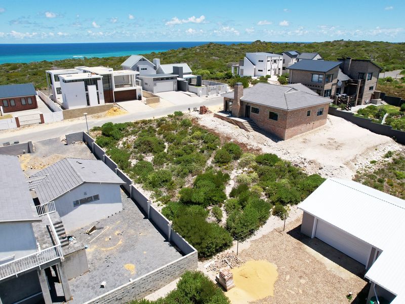Aerial view of a residential vacant land plot situated within a coastal estate, surrounded by established modern homes and natural vegetation.