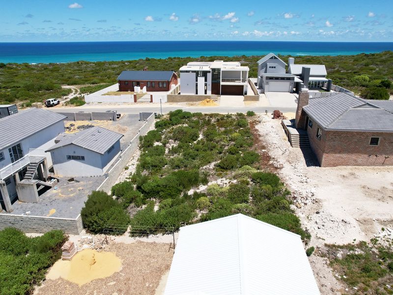 Aerial view of a vacant residential plot situated in a coastal neighborhood, surrounded by established homes and natural vegetation.