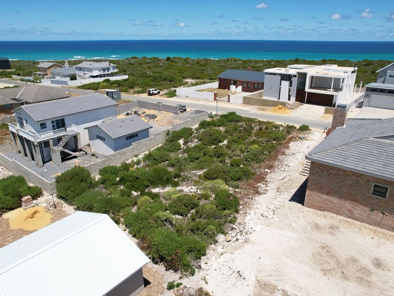 Aerial view of a vacant residential plot situated in a coastal neighborhood, offering proximity to the ocean and surrounding established homes.