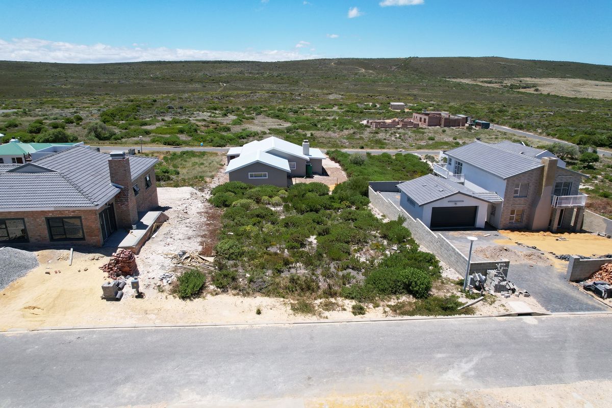 Aerial view of a vacant residential plot situated between existing homes, featuring natural vegetation and street access in a developing coastal estate.