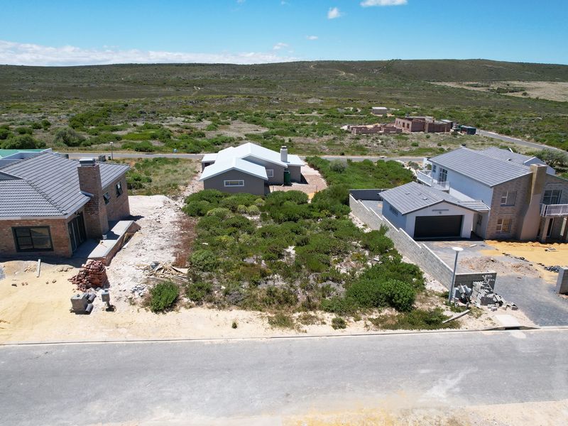 Aerial view of a vacant residential plot situated between existing homes, featuring natural vegetation and street access in a developing coastal estate.