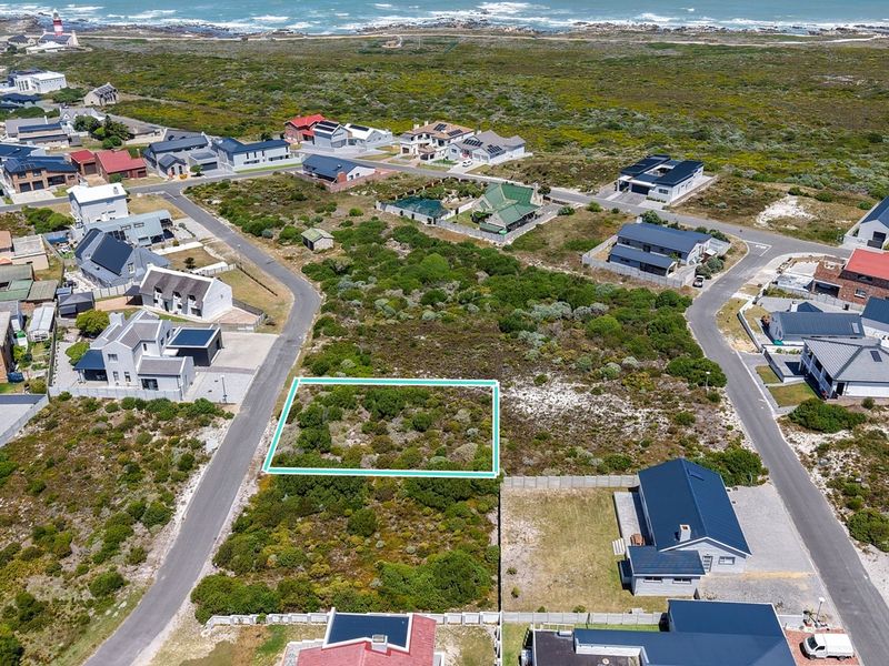 An aerial view of a vacant residential plot situated in a coastal neighborhood, highlighting the surrounding landscape and proximity to the ocean.