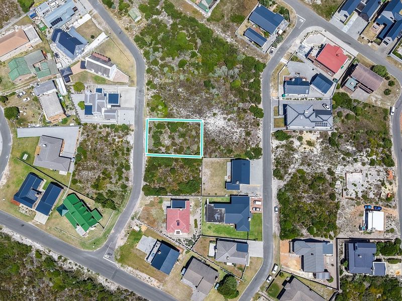 An aerial view of a vacant residential plot situated within a developed coastal neighborhood, featuring native vegetation and clear boundary markers.