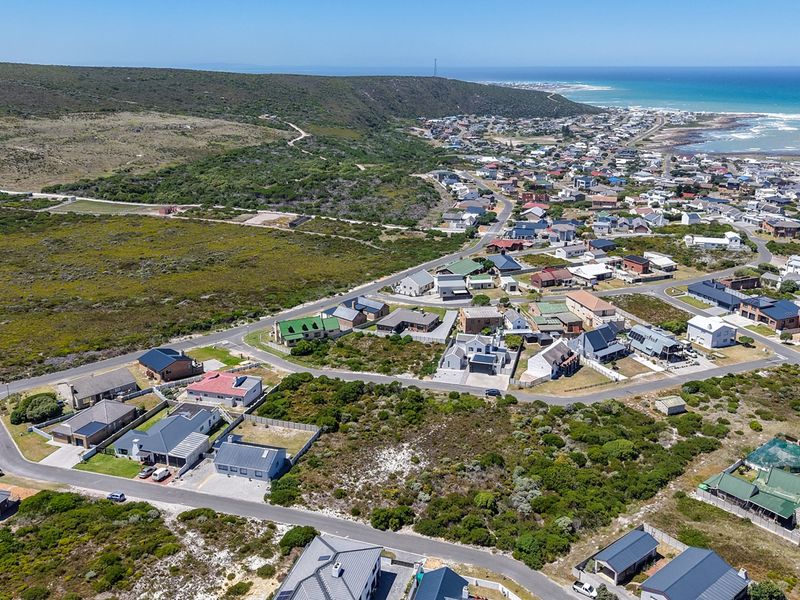 An aerial view of a coastal residential neighborhood showing surrounding vacant land, established housing, and proximity to the ocean.