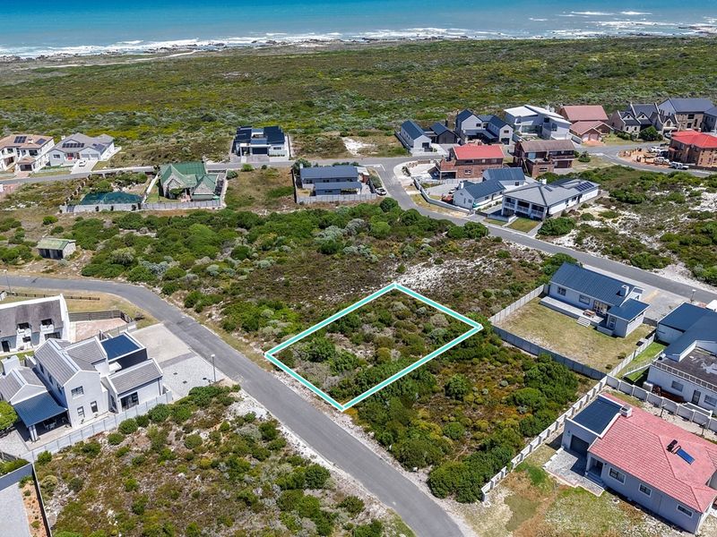 An aerial view of a vacant residential plot situated in a coastal neighborhood, featuring direct road access and proximity to the ocean.