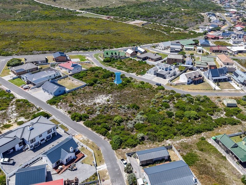 Aerial view of a vacant residential plot situated in a developed coastal neighborhood with established road access and surrounding residential properties.