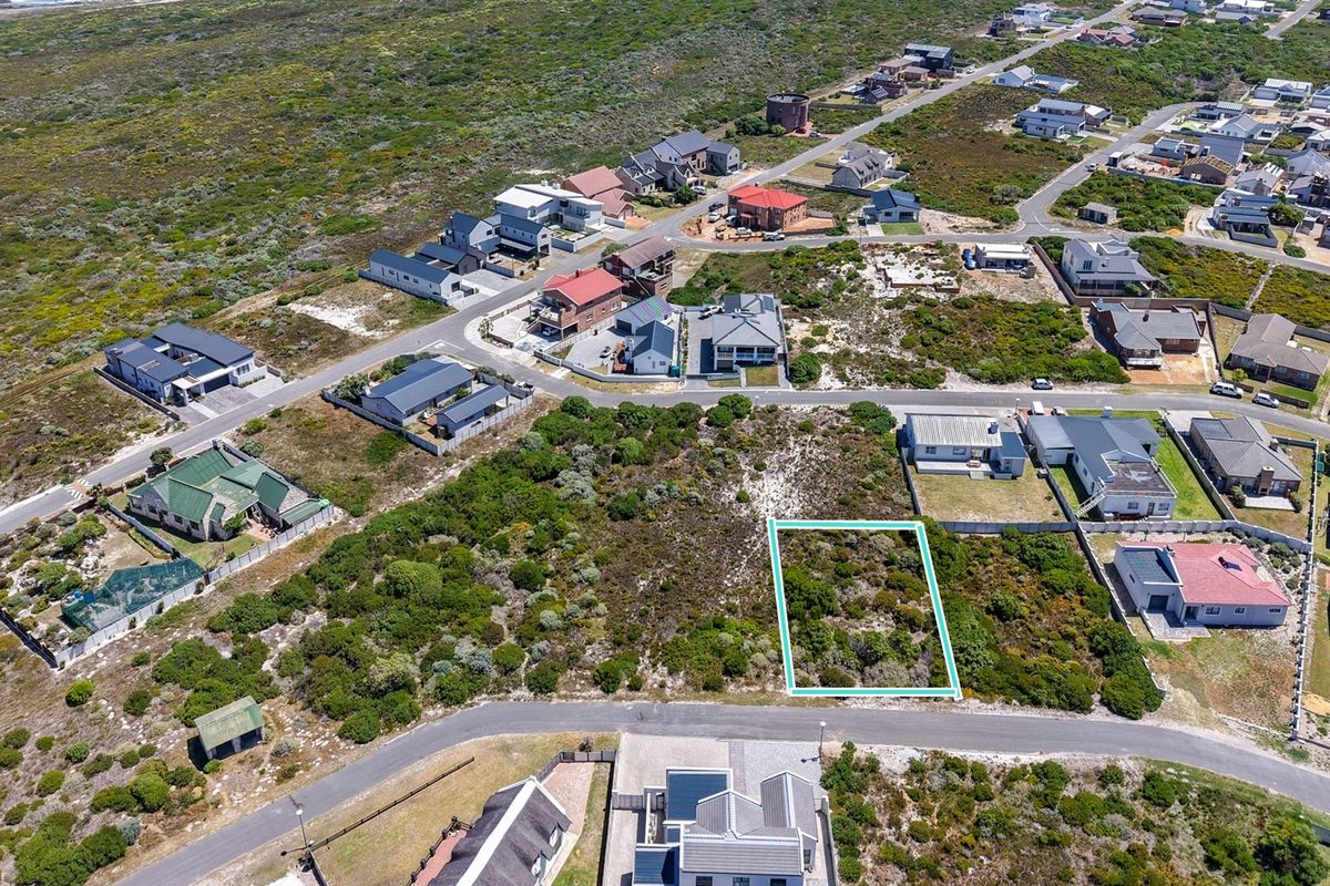 An aerial view of a vacant residential plot situated in a coastal neighborhood, highlighting the surrounding landscape and existing residential development.