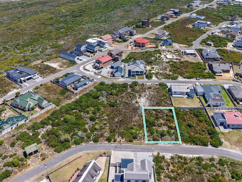 An aerial view of a vacant residential plot situated in a coastal neighborhood, highlighting the surrounding landscape and existing residential development.