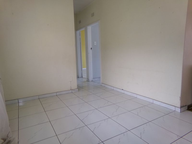 An empty hallway featuring white tiled flooring and neutral walls, providing access to adjacent rooms within the apartment.