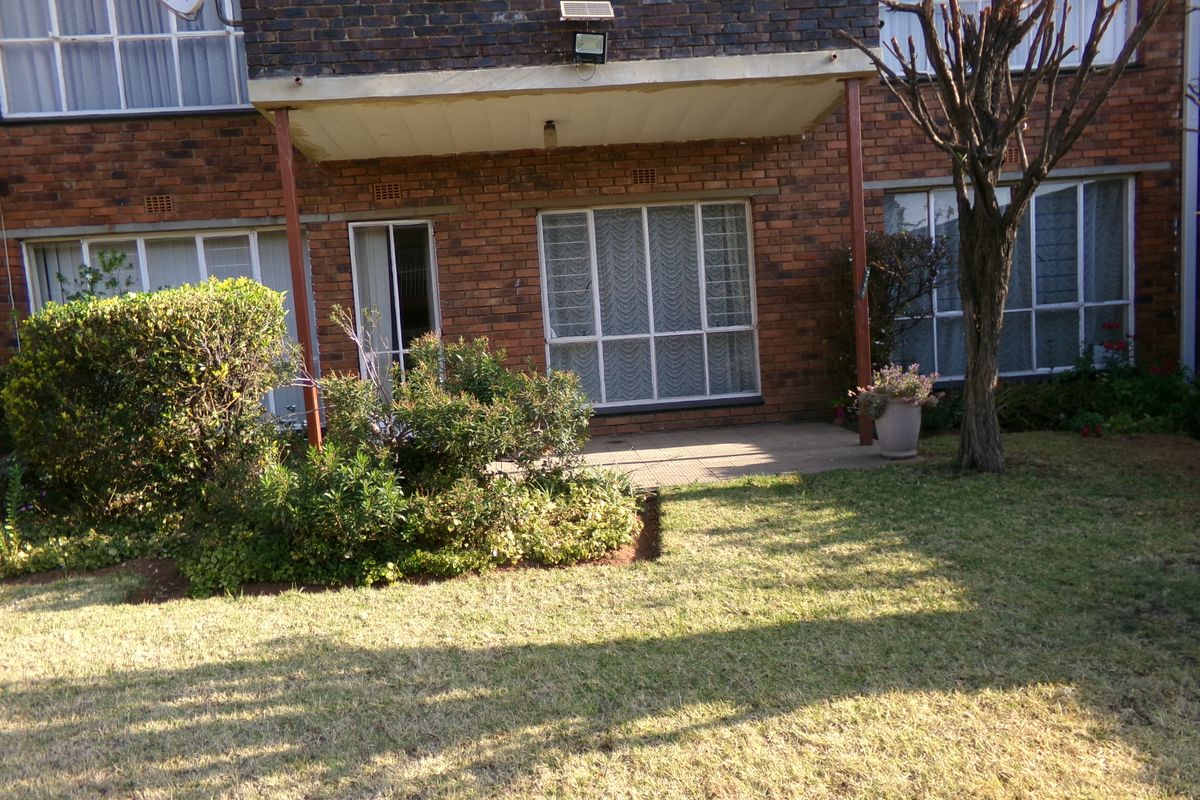 Rear view of the apartment building featuring a paved patio area, brick facade, and established garden space.