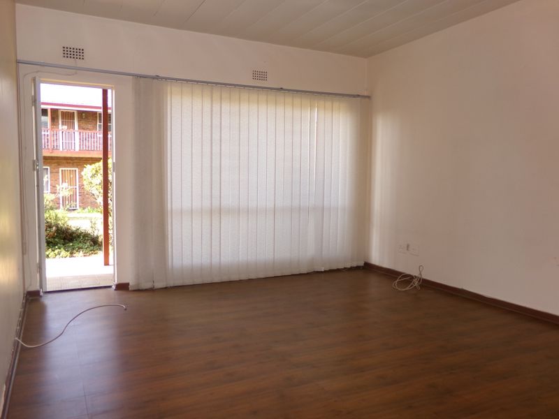 An empty, well-lit living room featuring laminate wood-look flooring, vertical blinds, and direct access to an outdoor patio area.