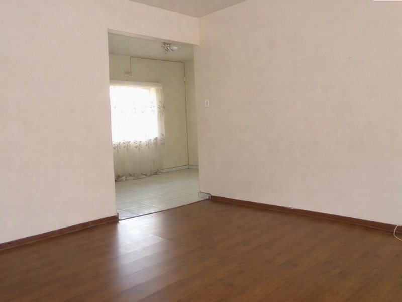 An empty living room featuring laminate flooring and neutral walls, with an open doorway leading to an adjacent tiled space.