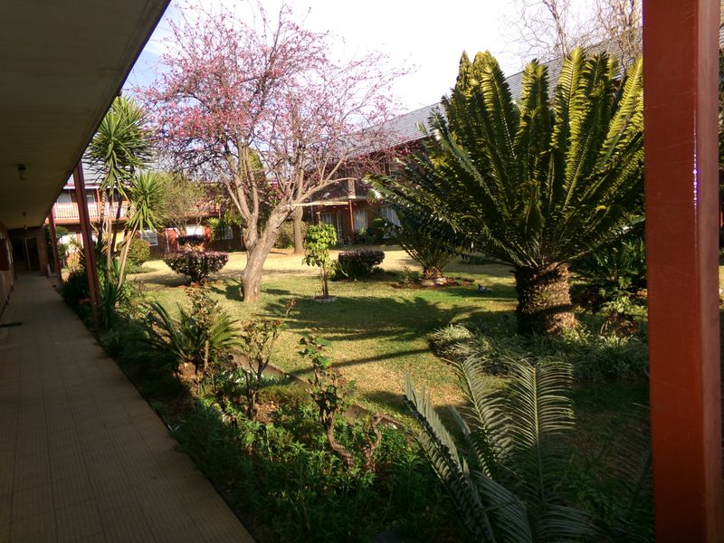 A view of a well-maintained communal garden area with mature trees and a covered paved walkway within an apartment complex.