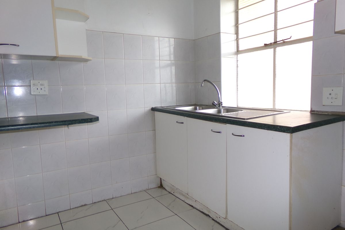 A functional, empty kitchen featuring white cabinetry, tiled splashbacks, a stainless steel sink, and tiled flooring, ready for a modern update.