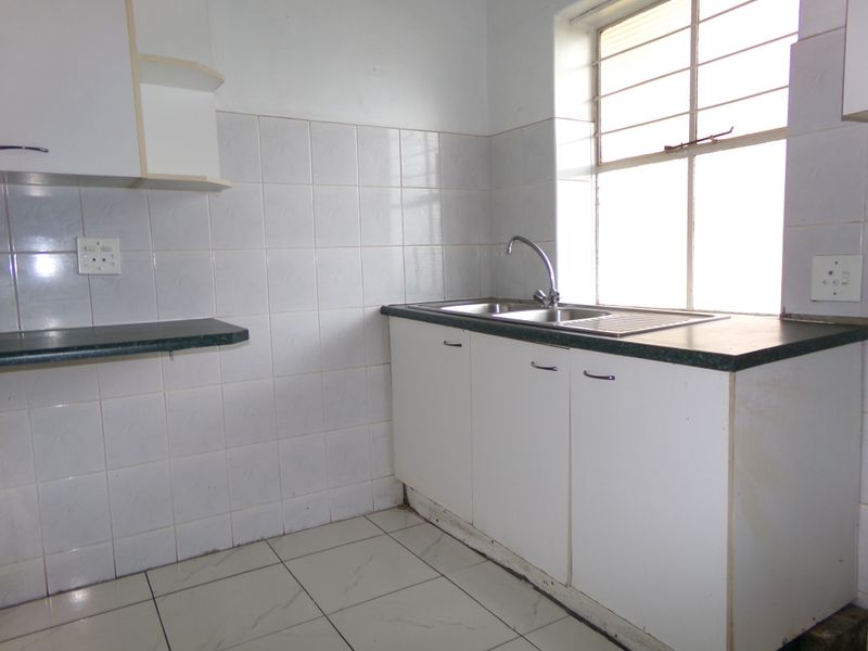 A functional, empty kitchen featuring white cabinetry, tiled splashbacks, a stainless steel sink, and tiled flooring, ready for a modern update.