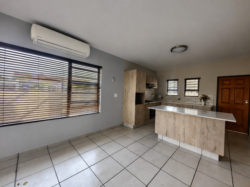 Modern kitchen featuring light wood-look cabinetry, stone countertops, a central island, tiled flooring, and an integrated air conditioning unit.