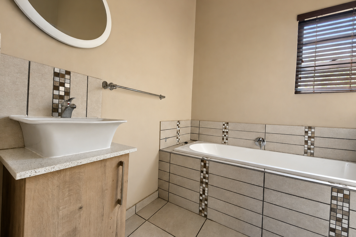 Modern bathroom featuring a vessel sink on a wood-finish vanity, a tiled built-in bathtub, and neutral wall tones with decorative mosaic tile accents.