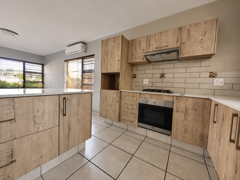 Modern kitchen featuring light wood-grain cabinetry, stone countertops, subway tile backsplash, integrated gas hob, electric oven, and a wall-mounted air conditioning unit.
