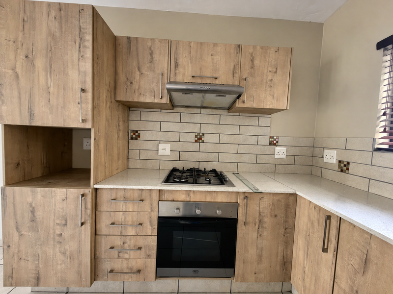 A modern kitchen featuring wood-look cabinetry, a built-in oven with gas hob, extractor fan, and subway tile backsplash with stone-look countertops.