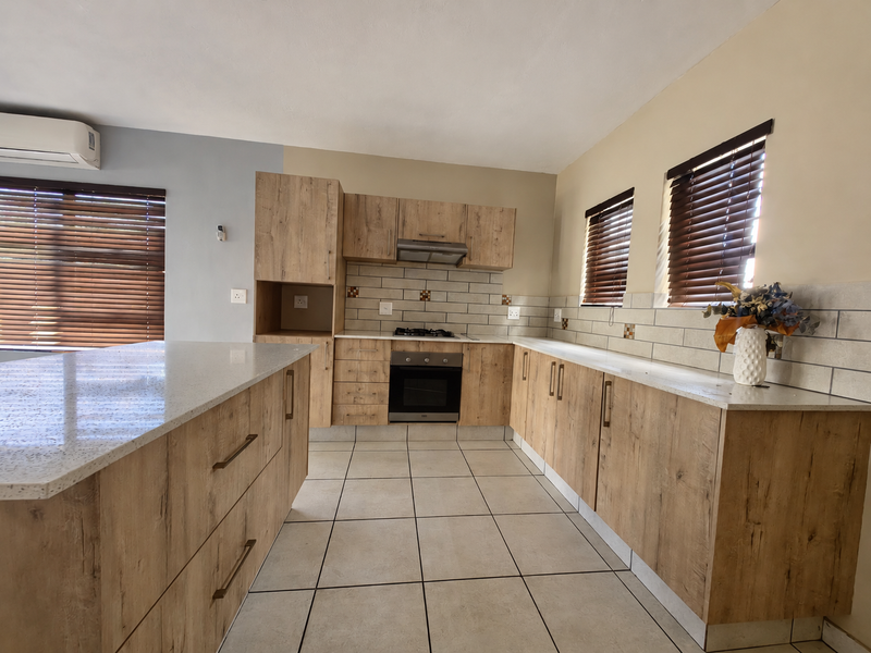 Modern kitchen featuring light wood-grain cabinetry, stone countertops, built-in oven, gas hob, extractor fan, and tiled flooring with ample natural light.