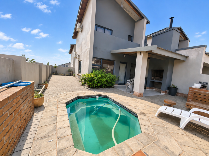 Rear exterior view of the townhouse featuring a paved patio, built-in braai area, and a private swimming pool.