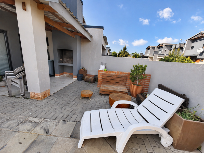 A paved outdoor patio area featuring a built-in braai, covered section, and low brick retaining wall, offering a functional space for outdoor entertainment.