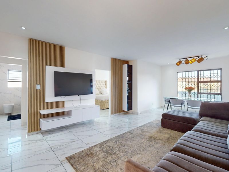 Spacious open-plan living and dining area featuring modern marble-look floor tiles, stylish timber wall paneling, and integrated media cabinetry.