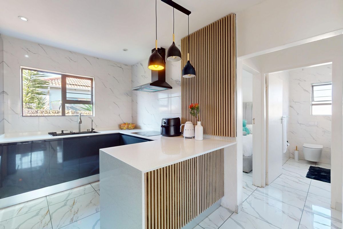 Modern kitchen featuring marble-look finishes, quartz countertops, sleek cabinetry, and a stylish slatted timber feature wall, with an adjacent bathroom visible.
