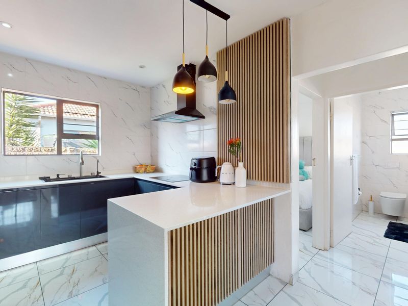 Modern kitchen featuring marble-look finishes, quartz countertops, sleek cabinetry, and a stylish slatted timber feature wall, with an adjacent bathroom visible.