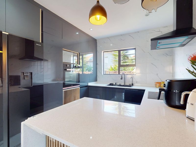Modern kitchen featuring high-gloss cabinetry, quartz countertops, marble-look splashback, built-in oven, and a stylish slatted wood accent wall.