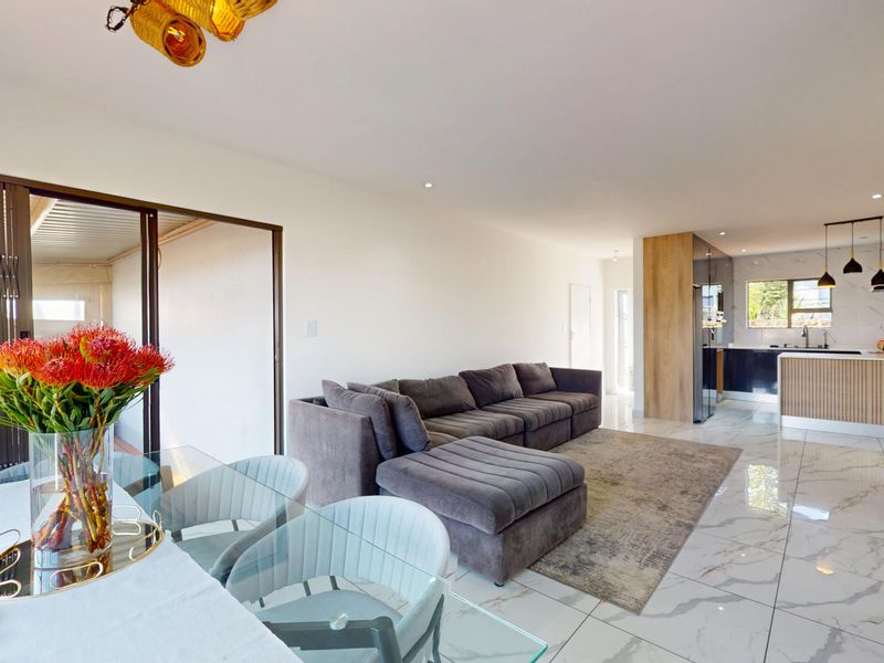 A bright open-plan living and kitchen area featuring modern marble-look floor tiles, sleek cabinetry, and seamless access to an outdoor patio space.