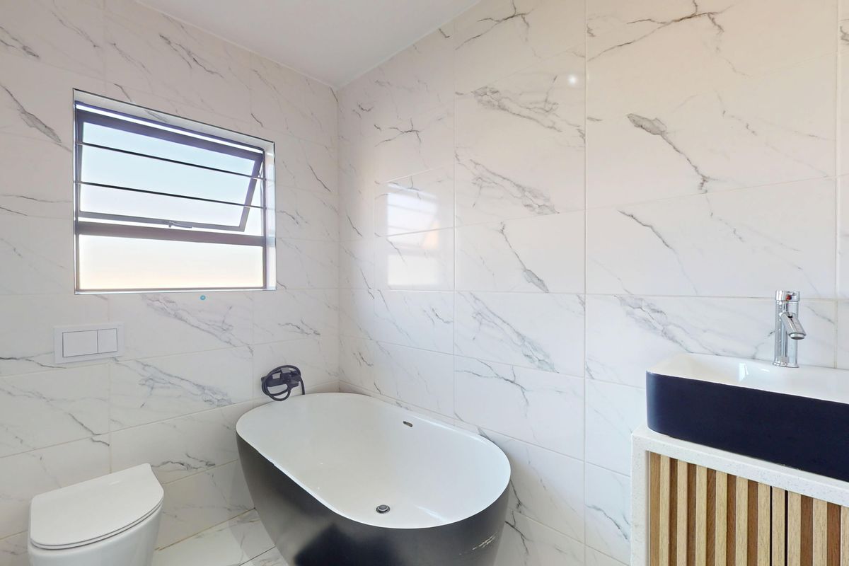 Modern bathroom featuring a sleek freestanding bathtub, wall-mounted toilet, and a contemporary vanity with marble-look wall tiling throughout.
