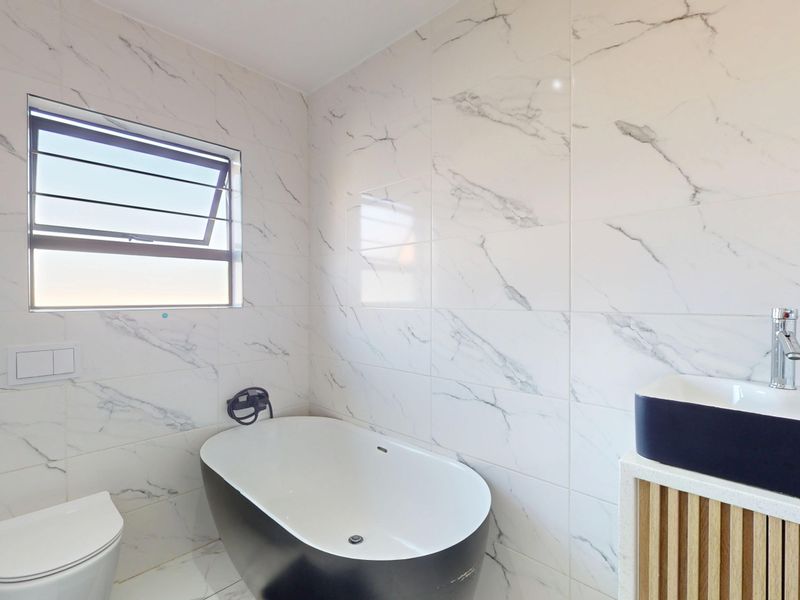 Modern bathroom featuring a sleek freestanding bathtub, wall-mounted toilet, and a contemporary vanity with marble-look wall tiling throughout.