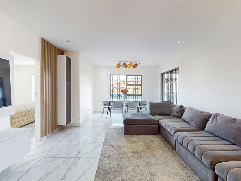 Spacious open-plan living and dining area featuring modern marble-look floor tiles, recessed lighting, and a decorative slatted timber wall accent.