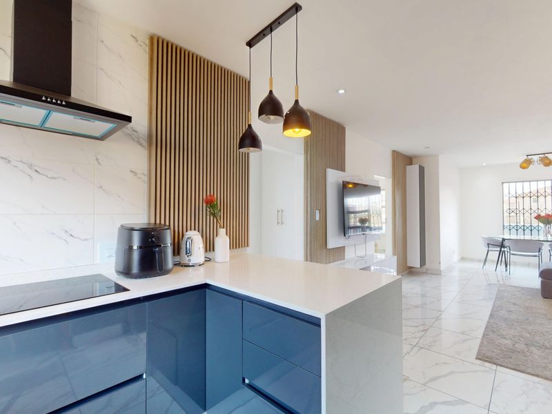 Modern open-plan living area featuring a sleek kitchen with glossy blue cabinetry, quartz countertops, marble-look flooring, and stylish slatted timber wall accents.
