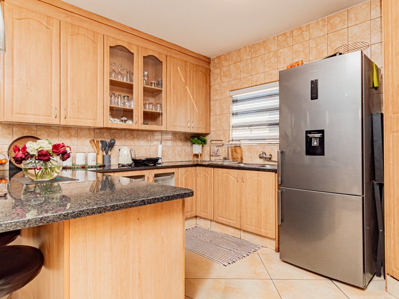 A functional kitchen featuring wooden cabinetry, granite countertops, tiled backsplash, and a breakfast bar area.